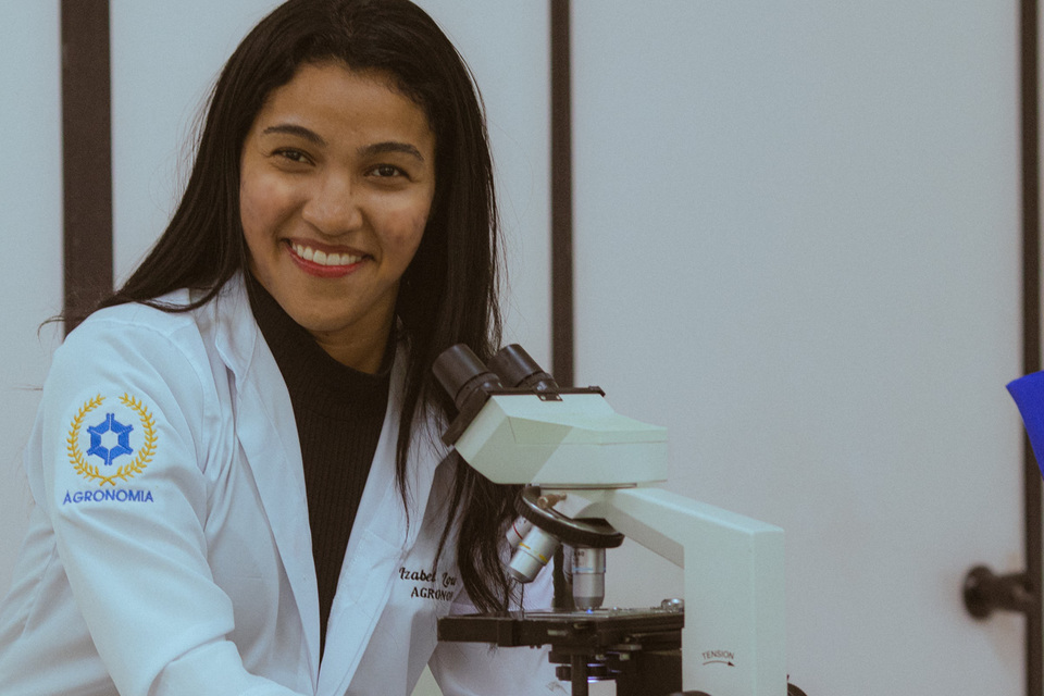 estudante de jaleco diante de um microscópio